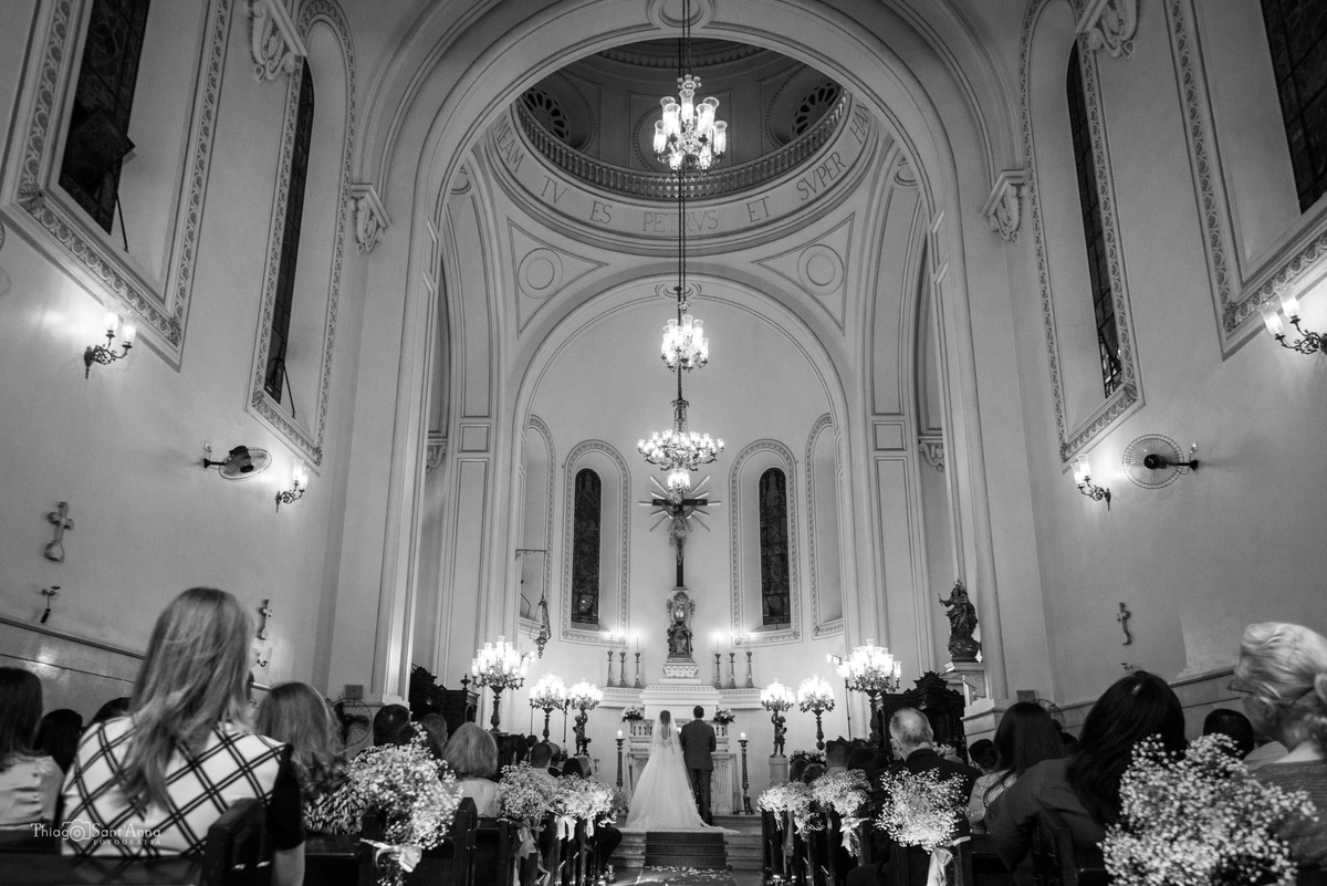 igreja católica lustres convidados sentados noivos no altar preto e branco