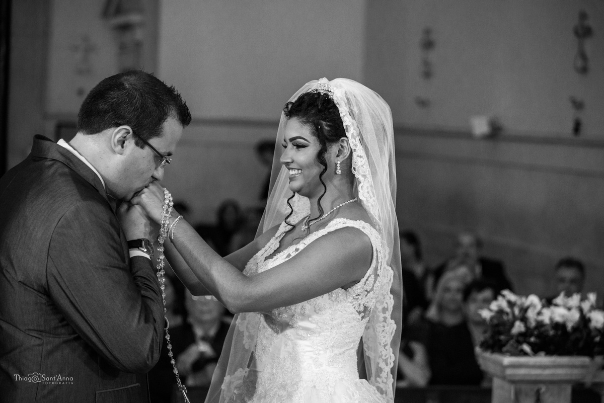 noivo beija mão da noiva sorri segura rosário preto e branco 