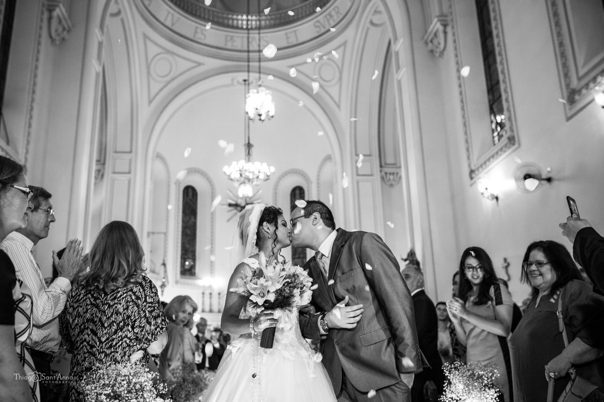 beijo dos noivos pétalas de rosa convidados observam preto e branco