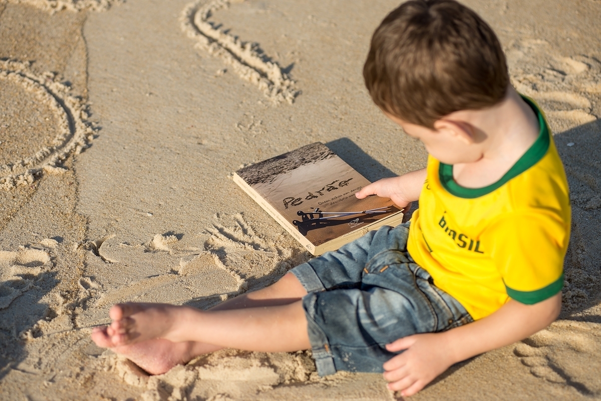 Menino com a camisa do brasil e seu livro na areia