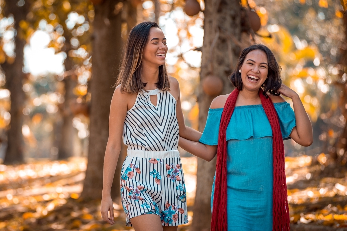 irmãs sorrindo caminham mãos dadas árvores folhas secas