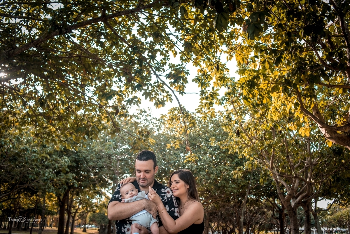 pais brincando com bebê em parque com muitas árvores