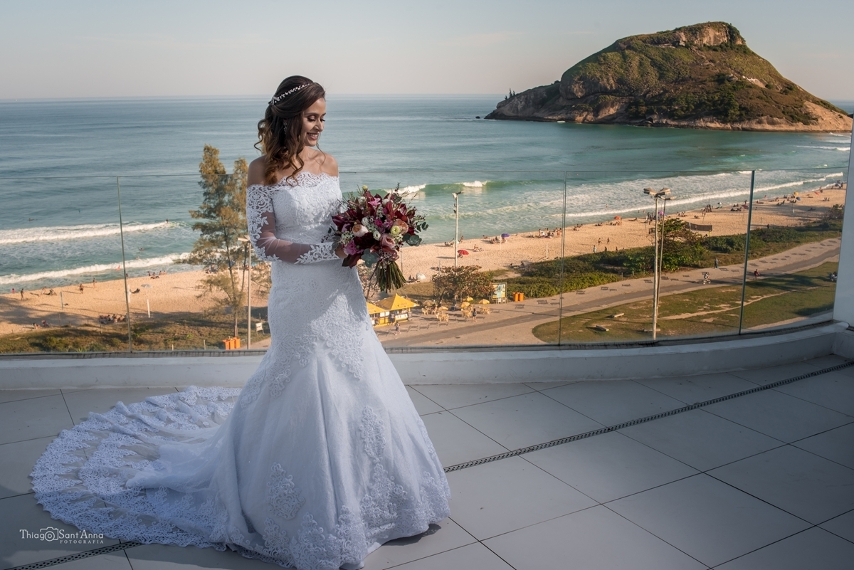 noiva olhando para o buquê na varanda do hotel no Recreio, com a orla ao fundo em Rio de Janeiro