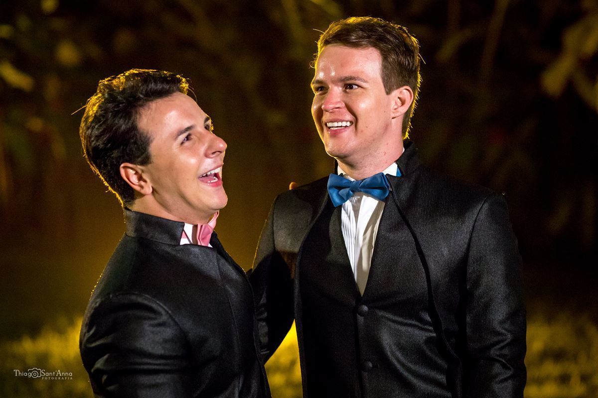 noivos abraçados sorrindo terno preto gravata borboleta rosa azul