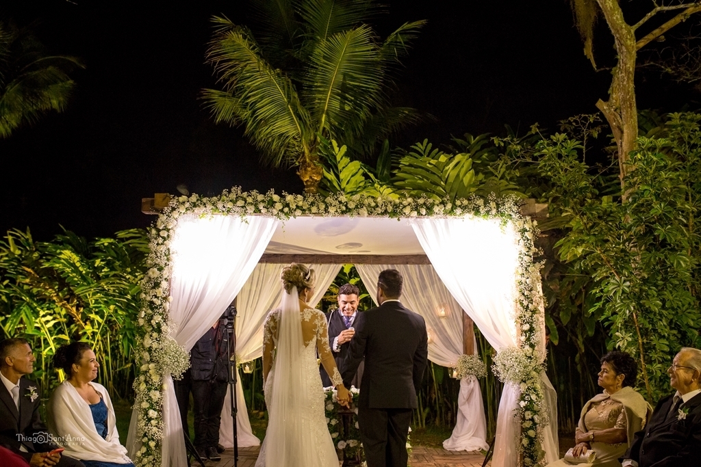 Fotografia dos noivos de costas em cerimônia de casamento no sítio ao ar livre a noite.