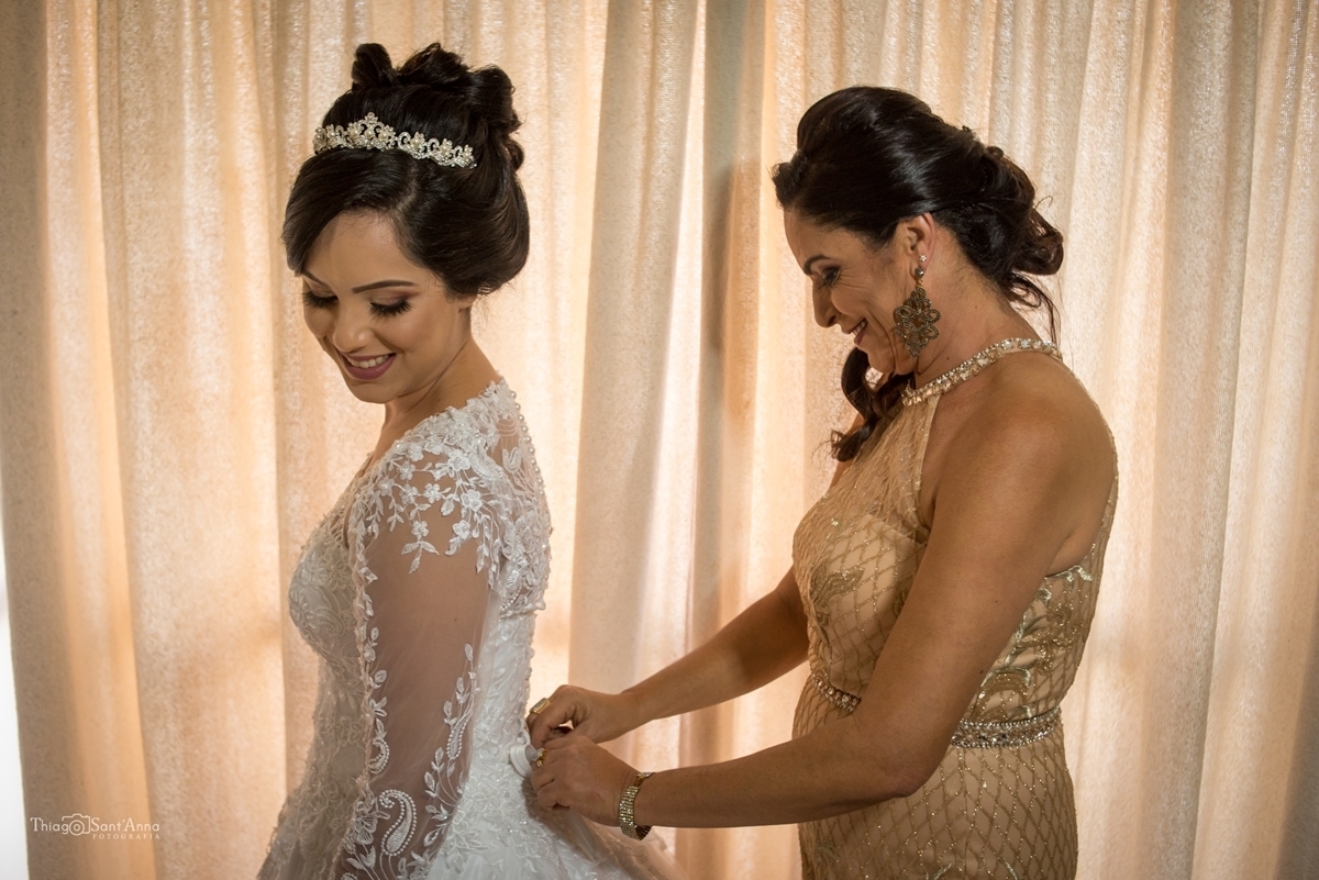 Mãe da noiva abotoando o vestido da filha