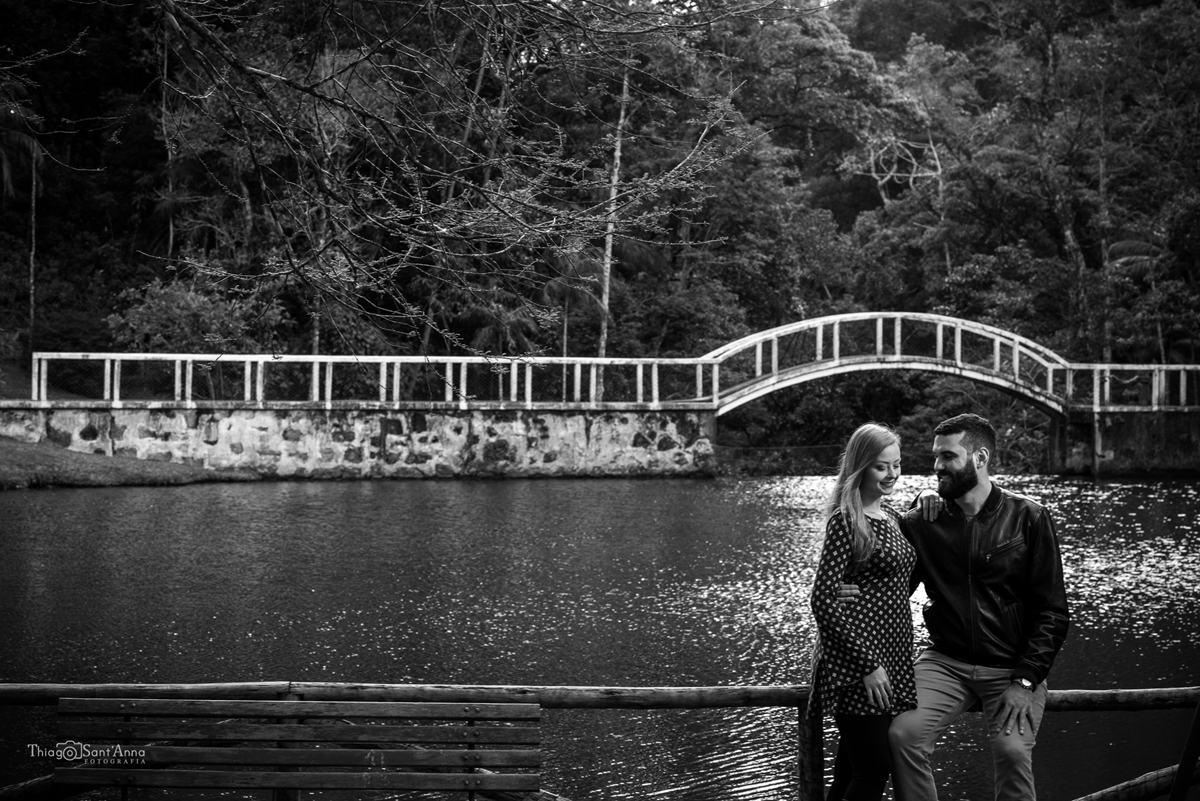 Fotografia de um casal em preto e branco a frente de uma ponte no parque