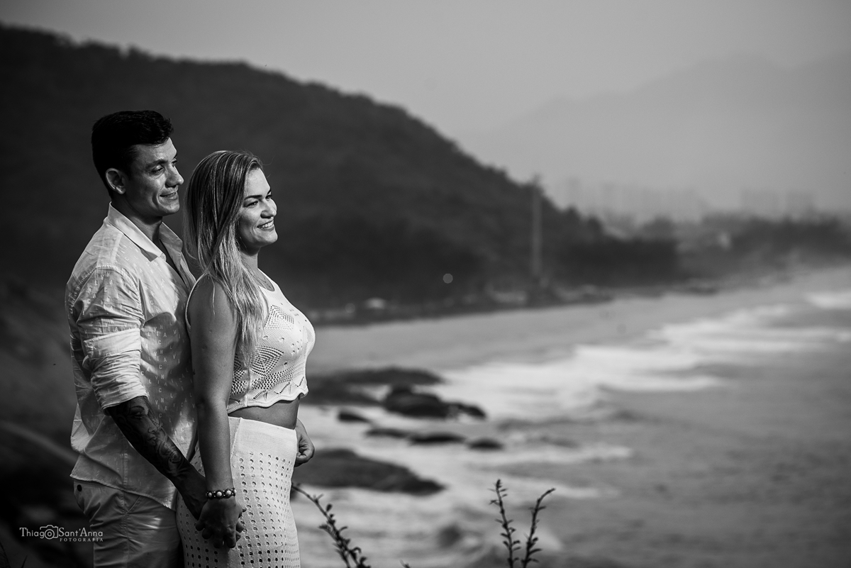 Fotografia de casal em preto e branco olhando para o horizonte com o mar ao fundo.