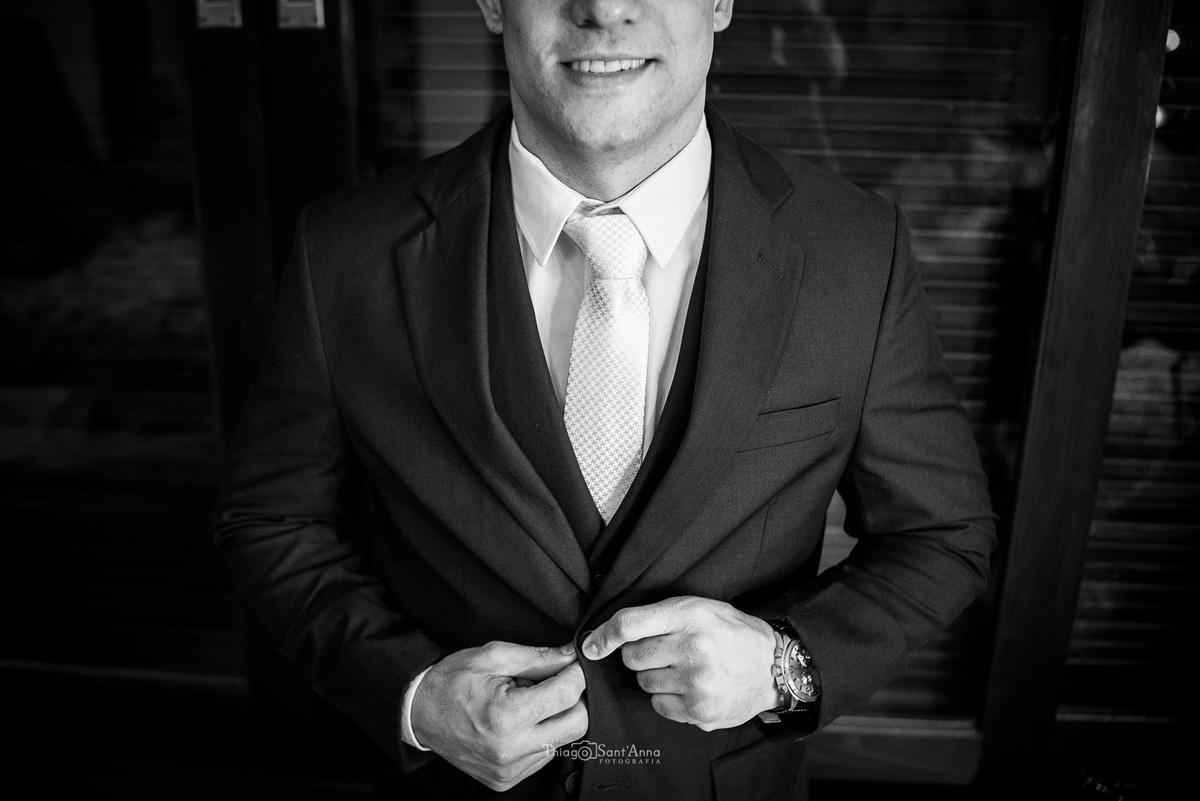noivo abotoa seu terno enquanto sorri preto e branco