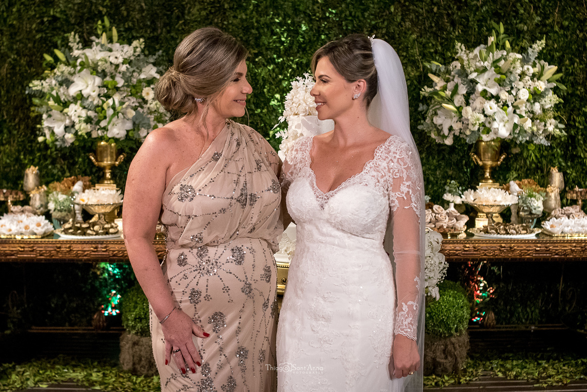 noiva e mãe da noiva abraçam decoração dourado parede viva flores brancas