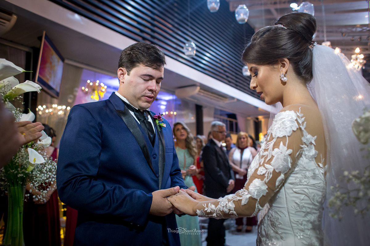 noivo segura as mão da noiva, rezam de olhos fechados, junto ao pastor decoração copos de leite luminárias teto 