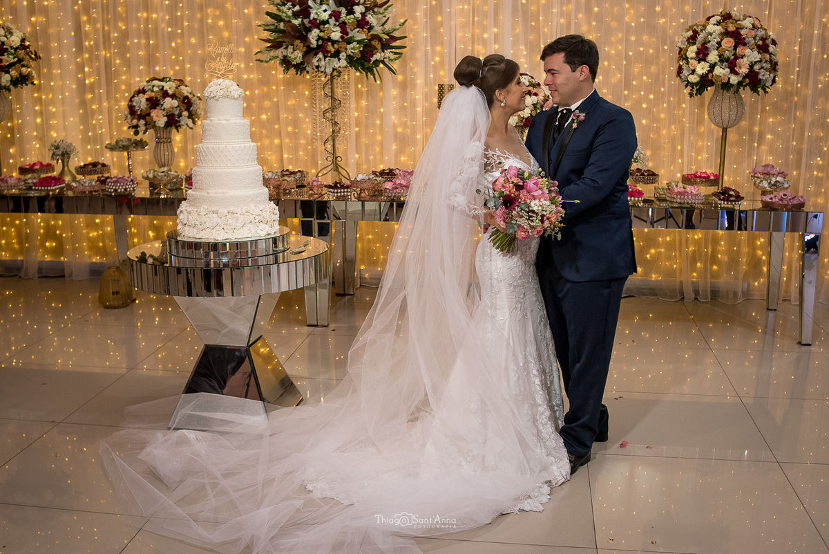 noivos se abraçam noiva vestido véu noivos se abraçam noiva véu buque tons de rosa noivo terno azul decoração flores coloridas tons de rosa bolo de casamento branco seis andares
