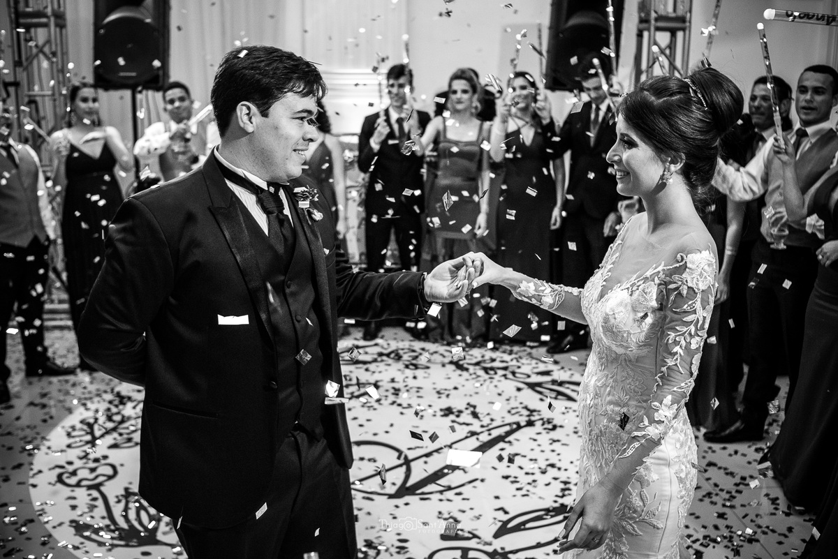 noivos dançam sob a queda do confete padrinhos em volta observam preto e branco