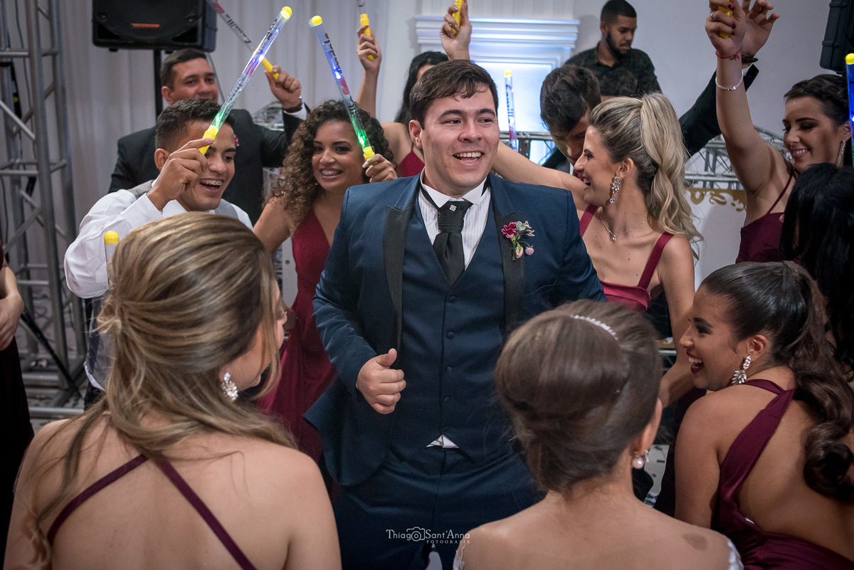 noivo sorri e dança entre madrinhas e padrinhos que seguram bastões luminosos