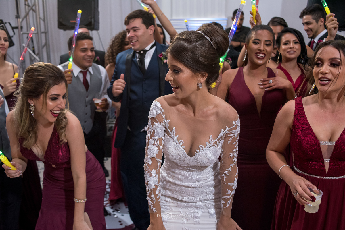 noiva sorri e dança entra madrinhas e padrinhos que seguram bastões luminosos noivo ao fundo 