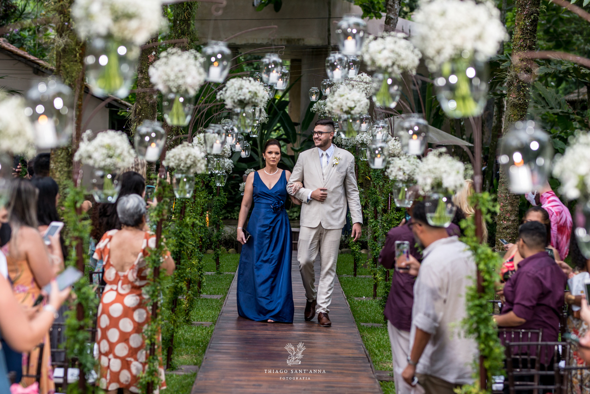 entrada do noivo terno bege vestido azul convidados observam de pé decoração jarros de flores brancas pendurados 