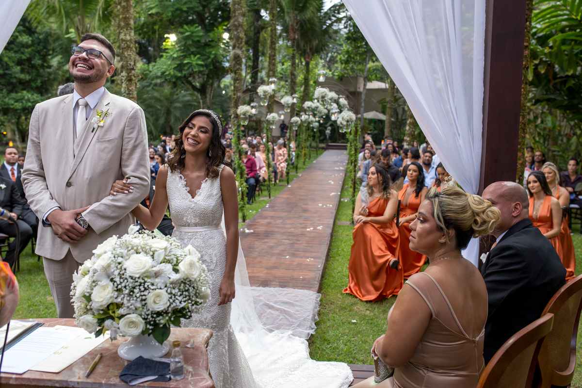 noivos sorrindo no altar convidados ao fundo ambiente externo decoração flores brancas