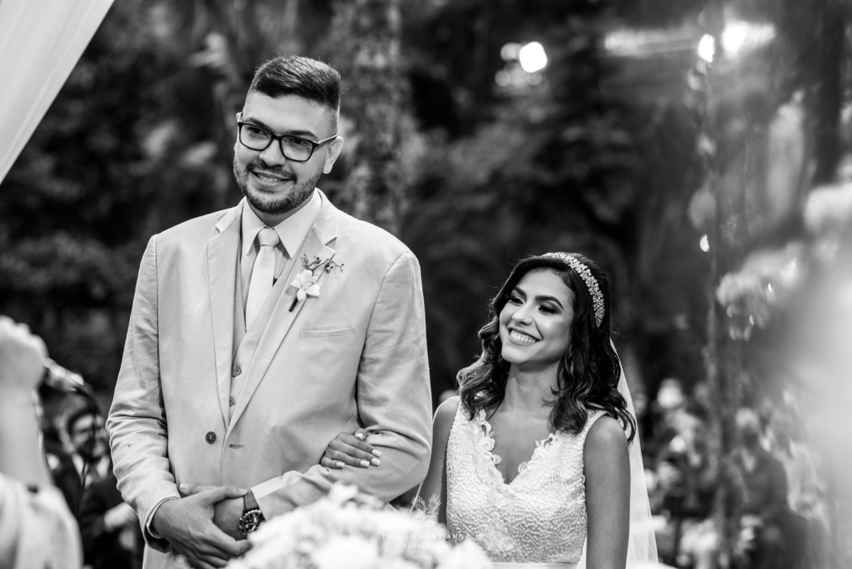 noivos sorrindo no altar ambiente externo decoração flores preto e branco