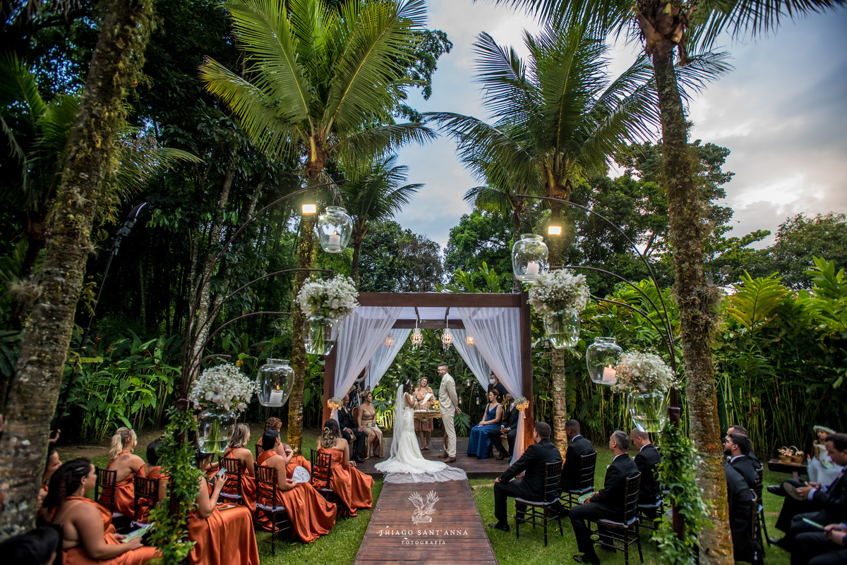 noivos no altar padrinhos observam observam ambiente externo decoração arranjos flores brancas vegetação palmeiras
