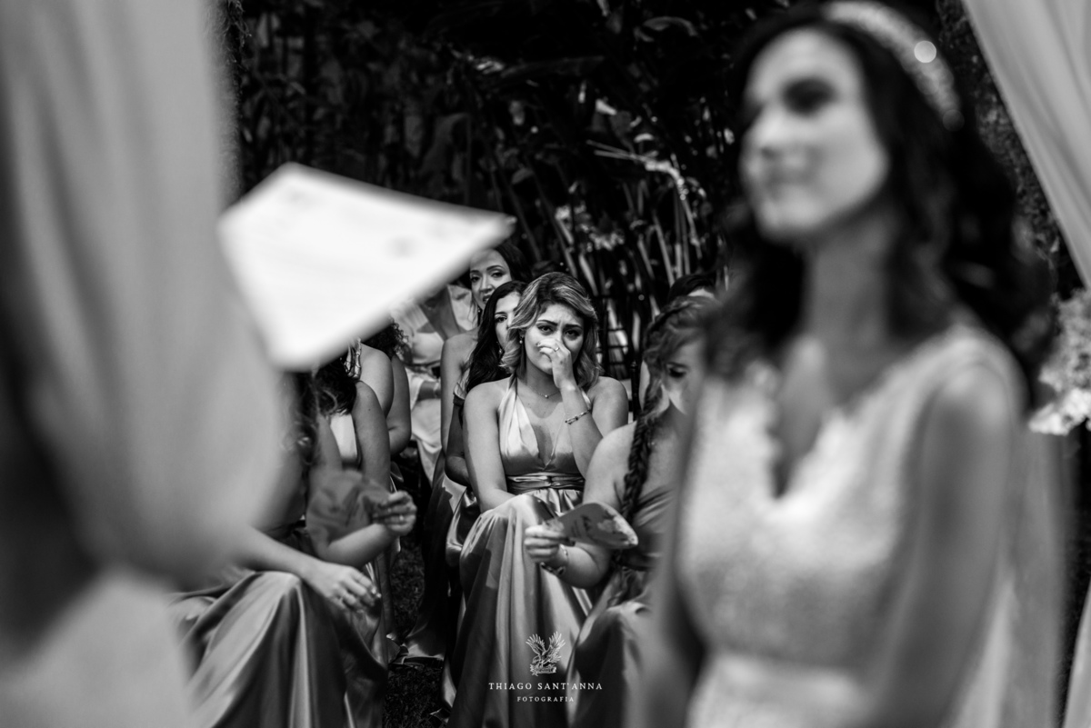 noiva atenta ao noivo que lê seus votos madrinhas ao fundo se emocionam preto e branco