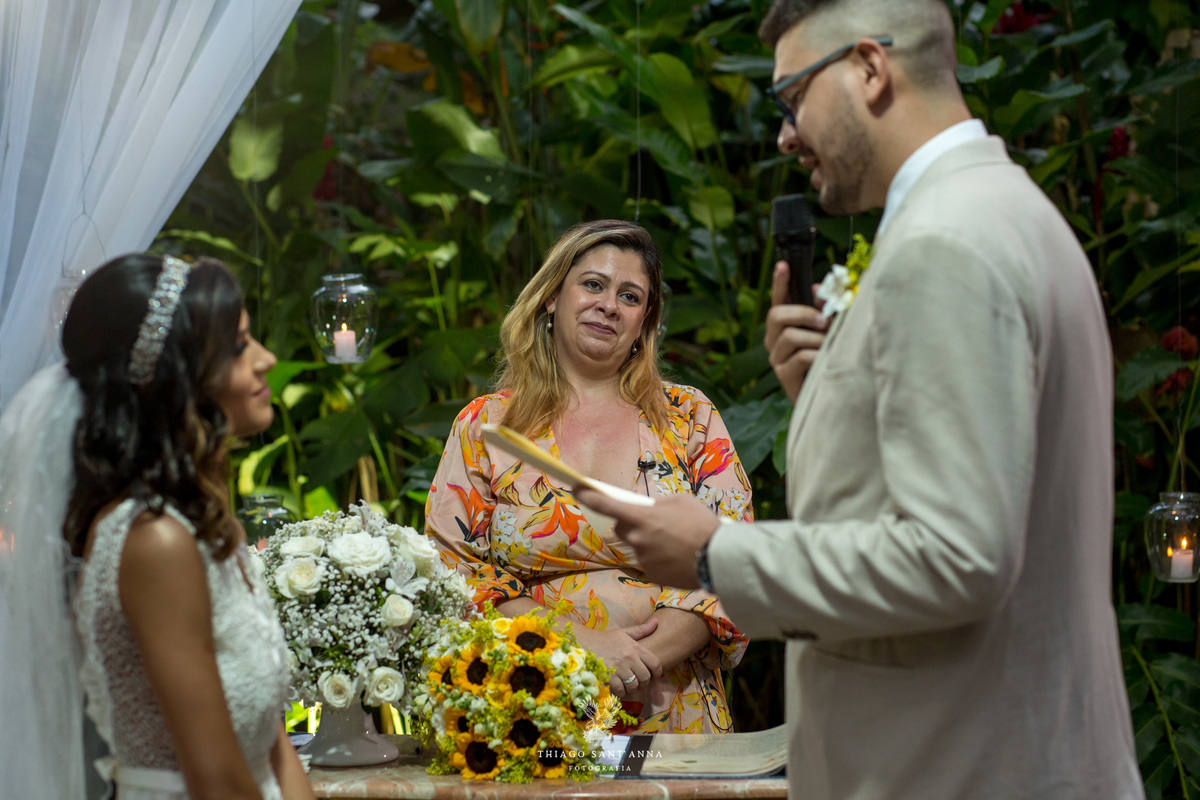 noivo lê seus votos noiva sorri pastora atenta fundo vegetação decoração flores brancas buque girassol