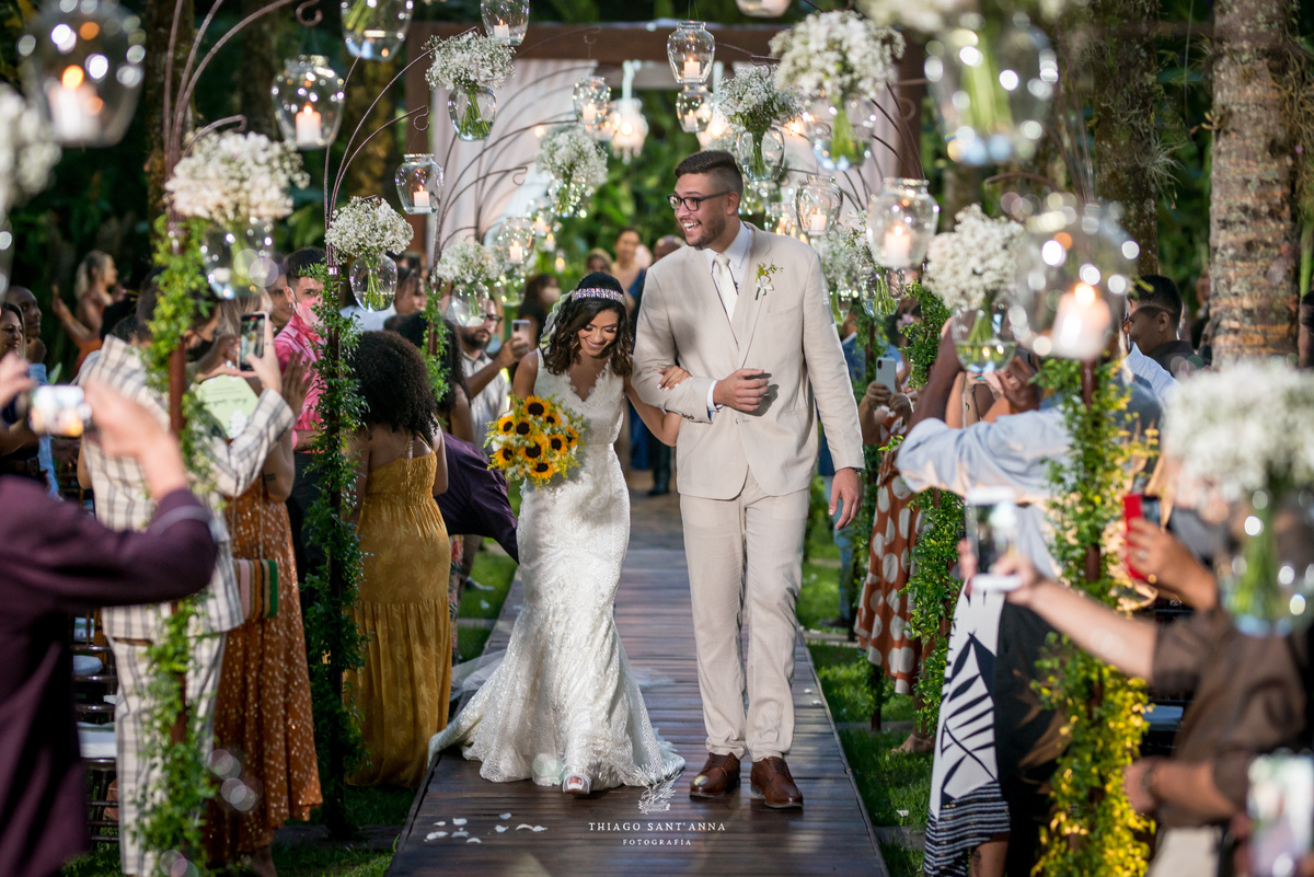 saída do casal sorriso noiva vestido buque girassol noivo terno bege ambiente externo vegetação arranjos flores brancas