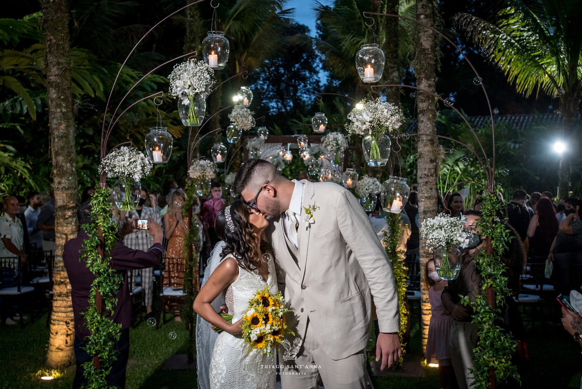 beijo do casal noiva vestido buque girassol noivo terno bege ambiente externo vegetação arranjos flores brancas