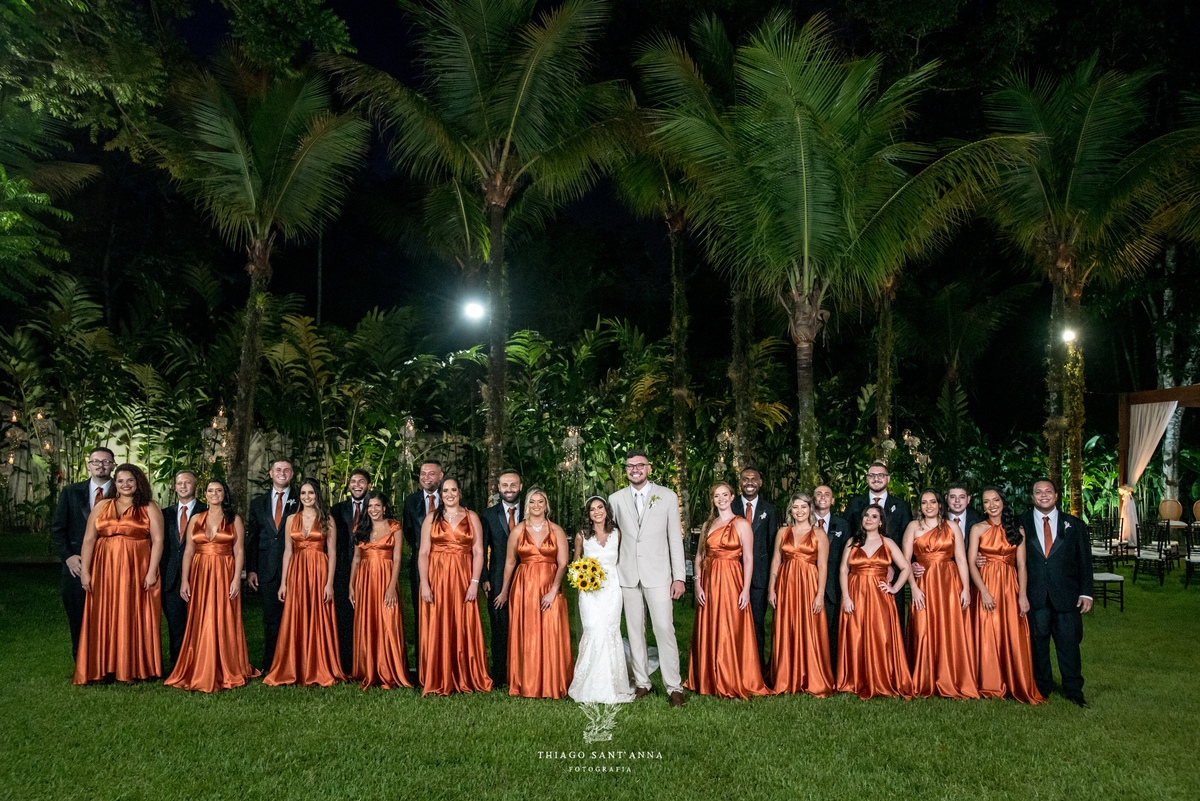 noivos posam com padrinhos terno preto e madrinhas vestido laranja cobre ambiente externo vegetação palmeiras gramado