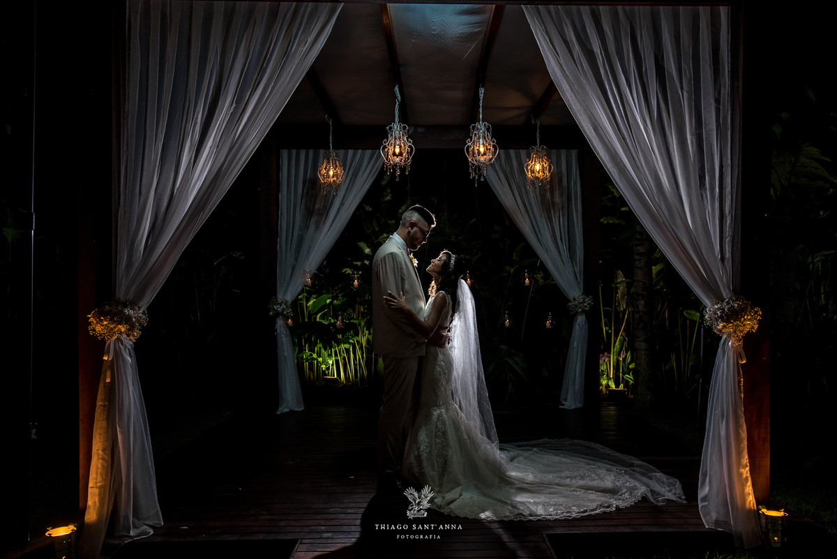 noivos posam abraçados silhueta cortinas brancas luminárias luz amarela