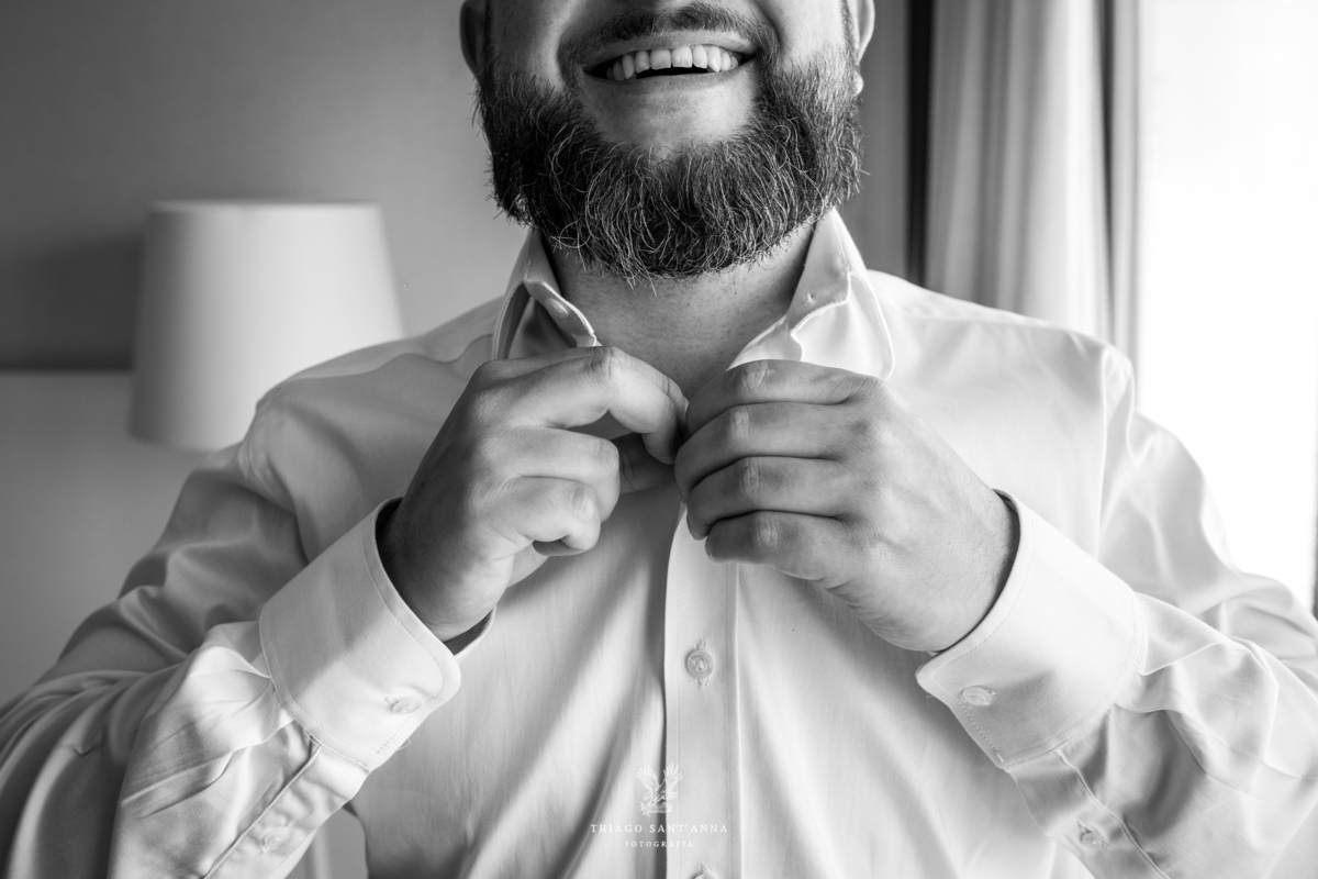 noivo se prepara casamento abotoa camisa sorrindo preto e branco