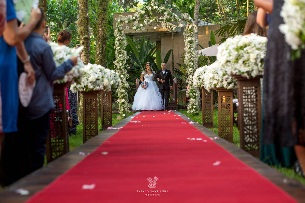 entrada da noiva com seu pai tapete vermelho decoração flores brancas convidados observam