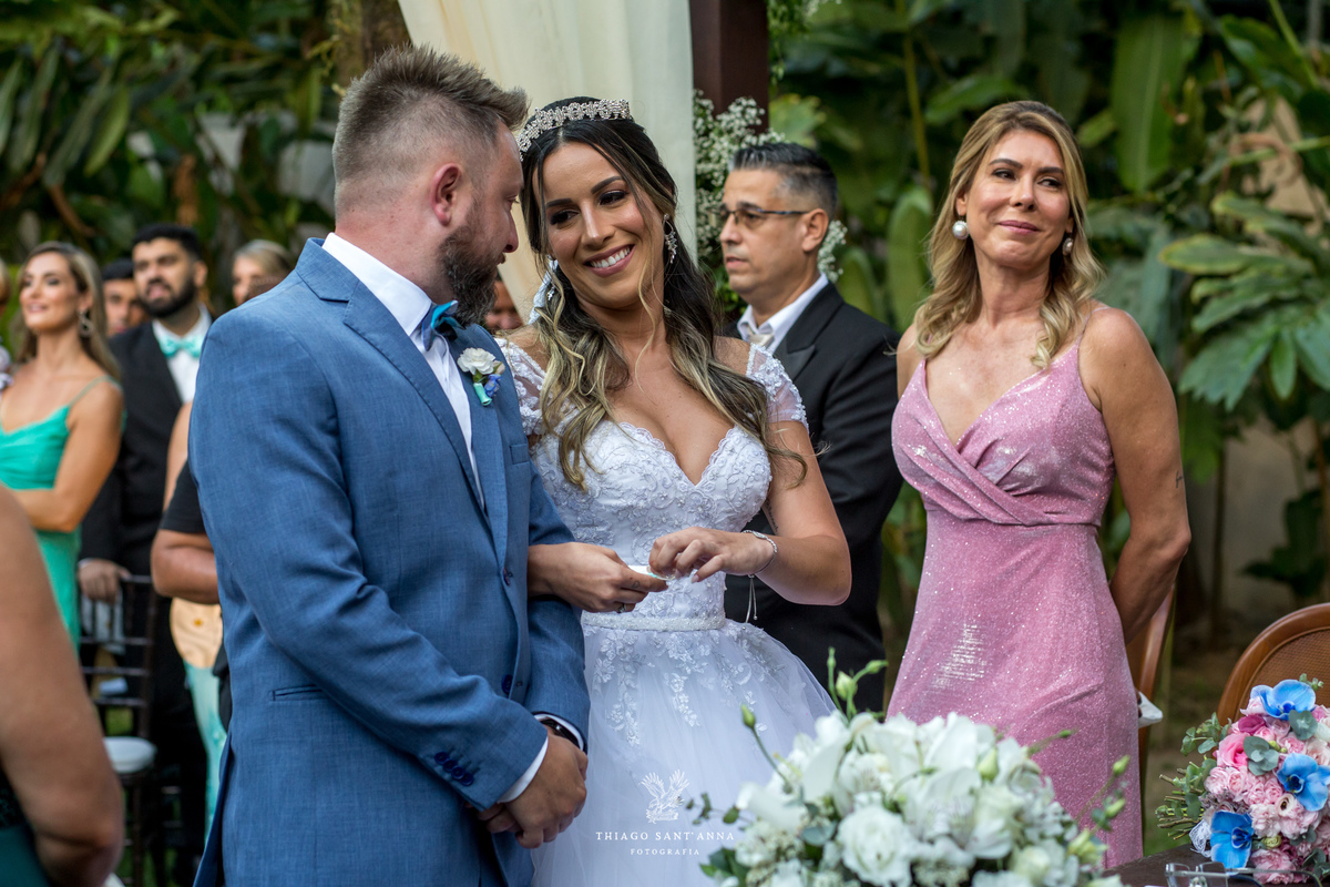 noivos altar sorrindo familiares observam flores decoração vegetação ao fundo