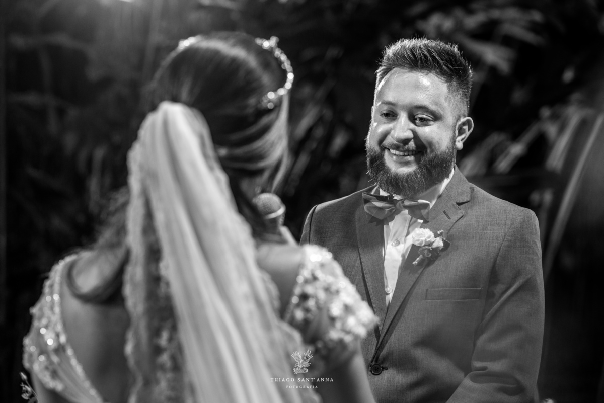 noivo sorri observando noiva falar ao microfone preto e branco