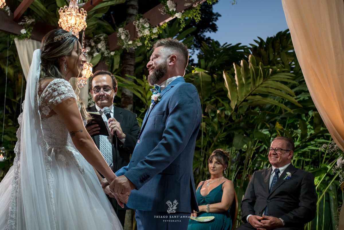 noivos de mãos dadas no altar frente a pastor familiares observam