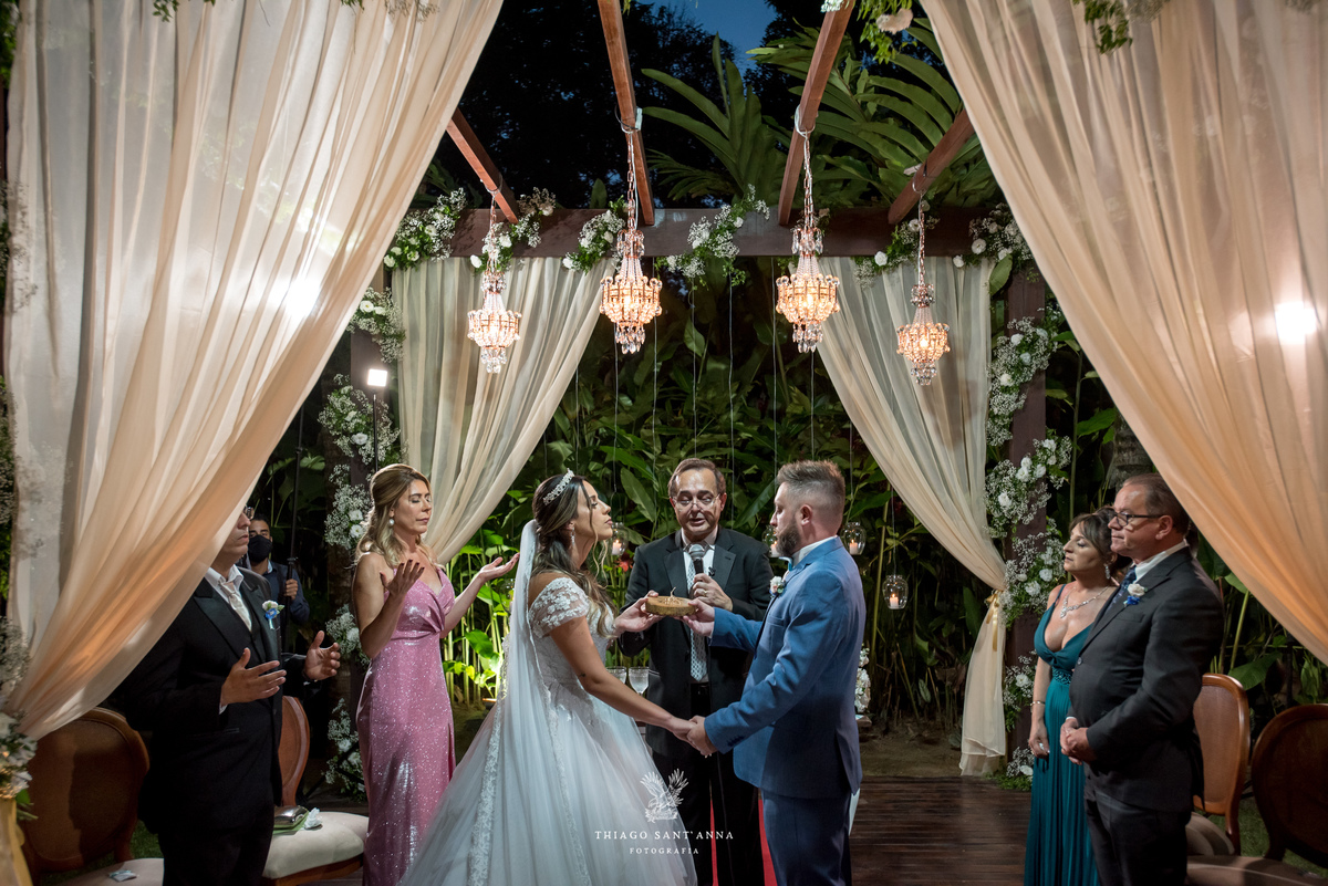 noivos de mãos dadas no altar frente a pastor familiares observam