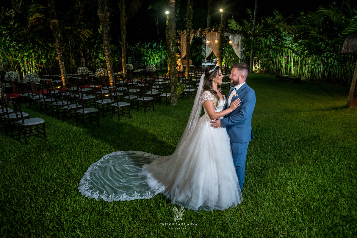 noivos abraçados ambiente externo vegetação flores brancas noivo terno azul noiva vestido renda 