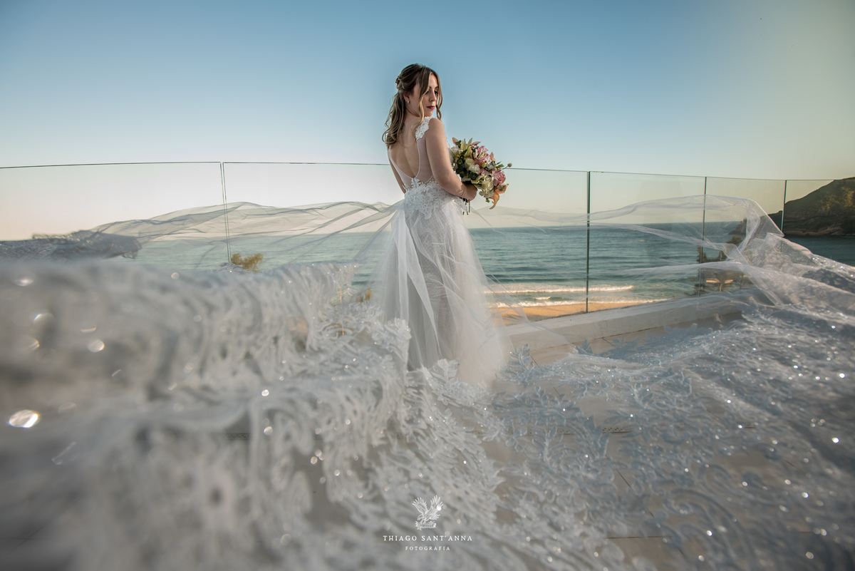 noiva vestido véu buque flores tons de rosa paisagem praia