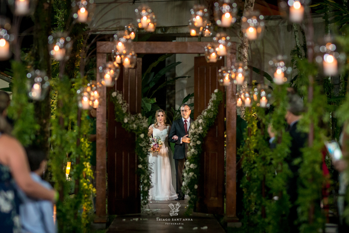 entrada da noiva com seu pai ambiente externo vegetação gramado árvores ao fundo decoração flores brancas luminárias velas