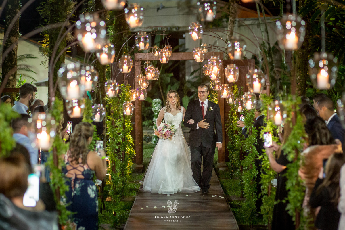 entrada da noiva com seu pai ambiente externo vegetação gramado árvores ao fundo decoração flores brancas luminárias velas