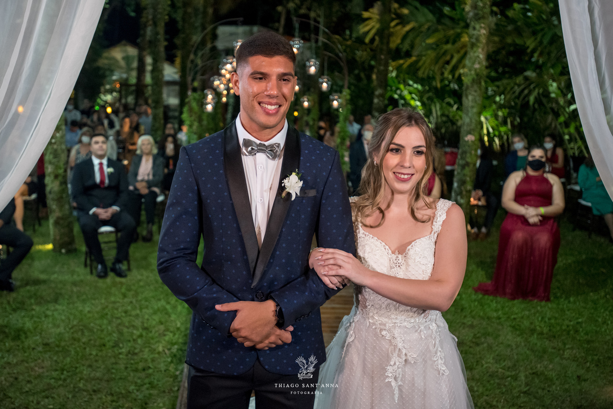 noivos sorrindo no altar vegetação gramado padrinhos ao fundo