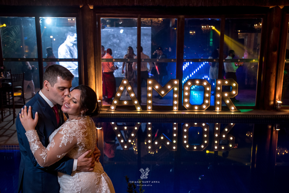 noivo beija rosto da noiva próximo a piscina letreiro luminoso ao fundo