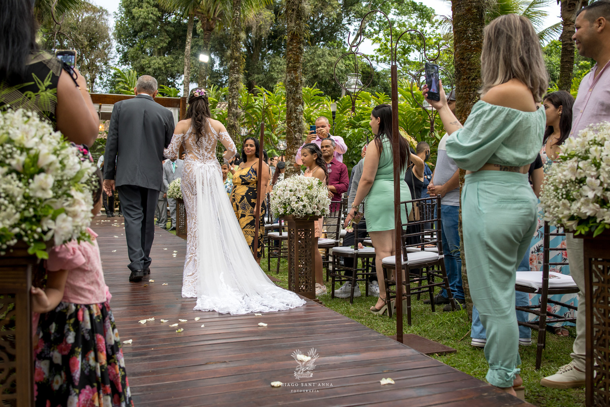 entrada noiva e seu pai convidados observam de pé decoração flores brancas ambiente externo vegetação gramado 