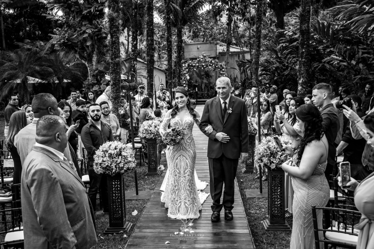 entrada noiva e seu pai convidados observam de pé decoração flores ambiente externo vegetação gramado preto e branco