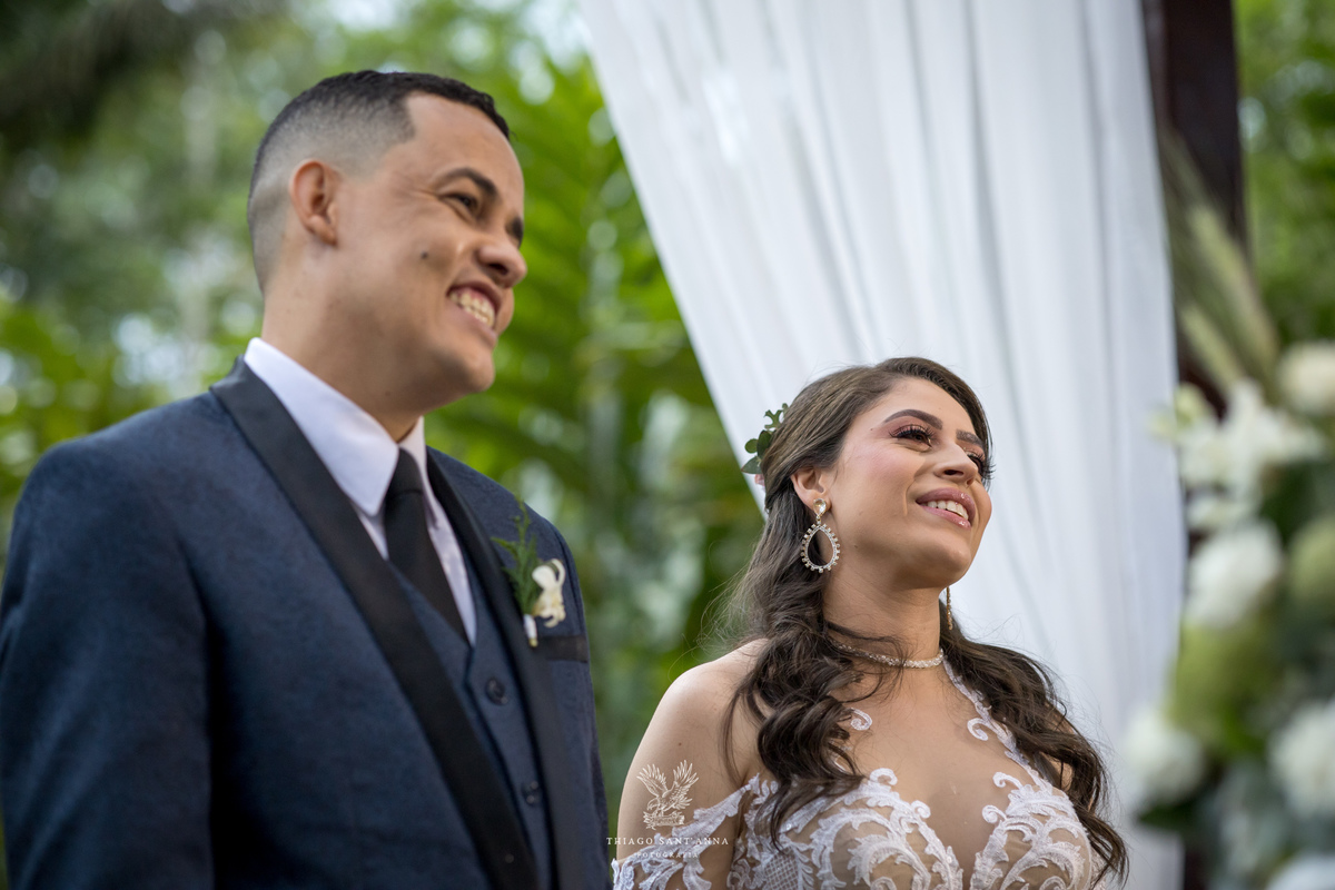 noivos no altar sorrindo se admiram estrutura de madeira tecido branco 