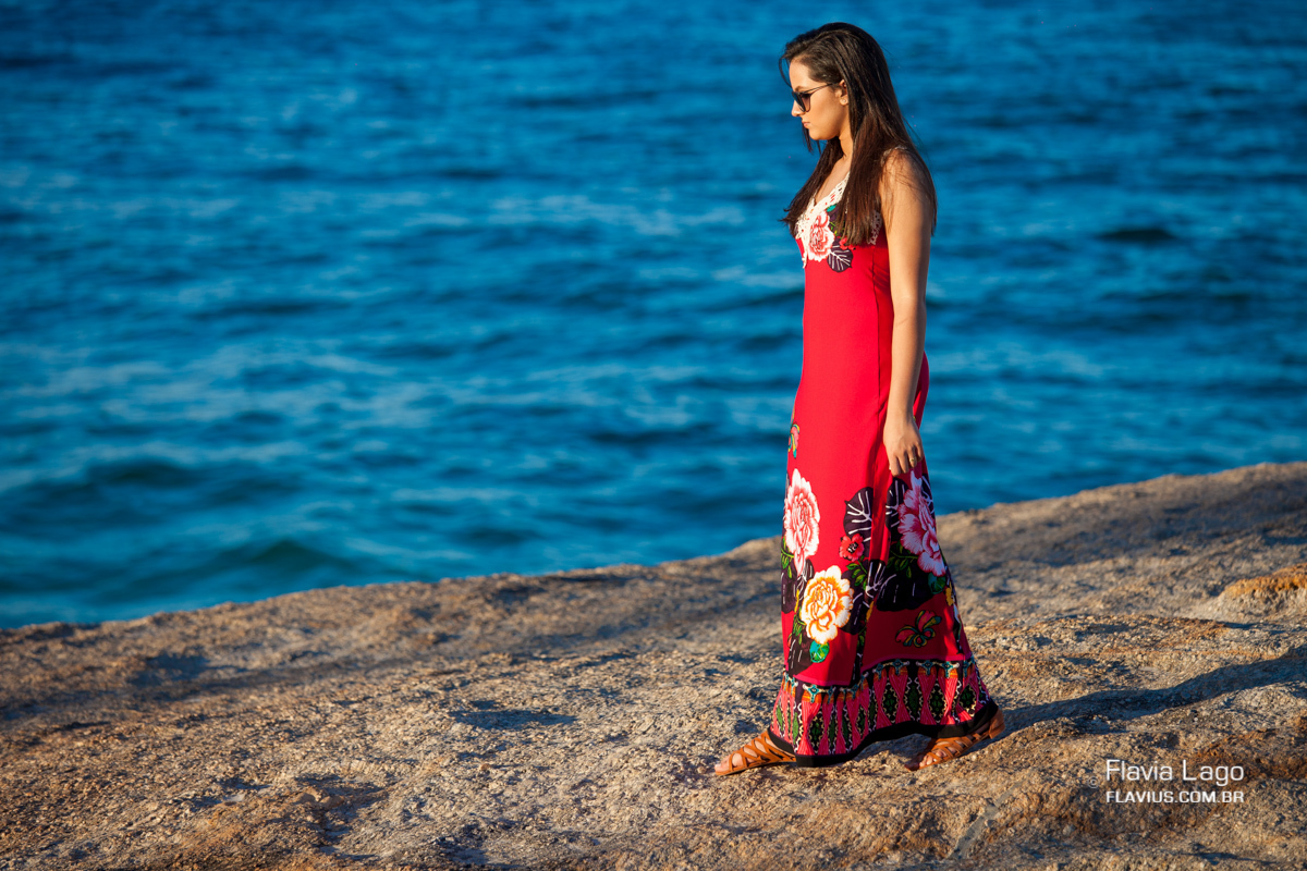 A debutante sobre o penhasco olhando para o mar posa para seu ensaio de 15 anos na praia pela fotógrafa de debutantes Flavia Lago no Rio de Janeiro - RJ
