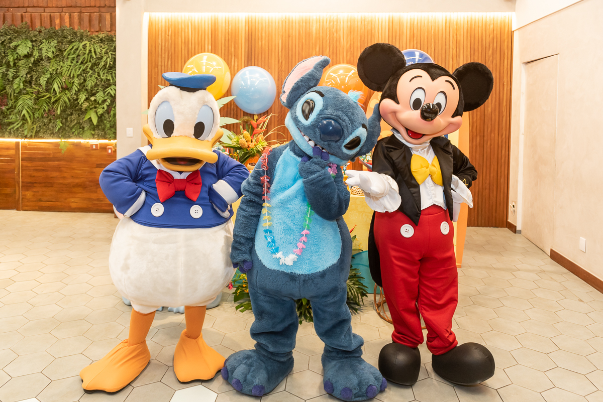 Personagens vivos Mickey Mouse, Pato Donald e Stitch em festa infantil, animação com personagens em buffet com decoração temática e balões coloridos.