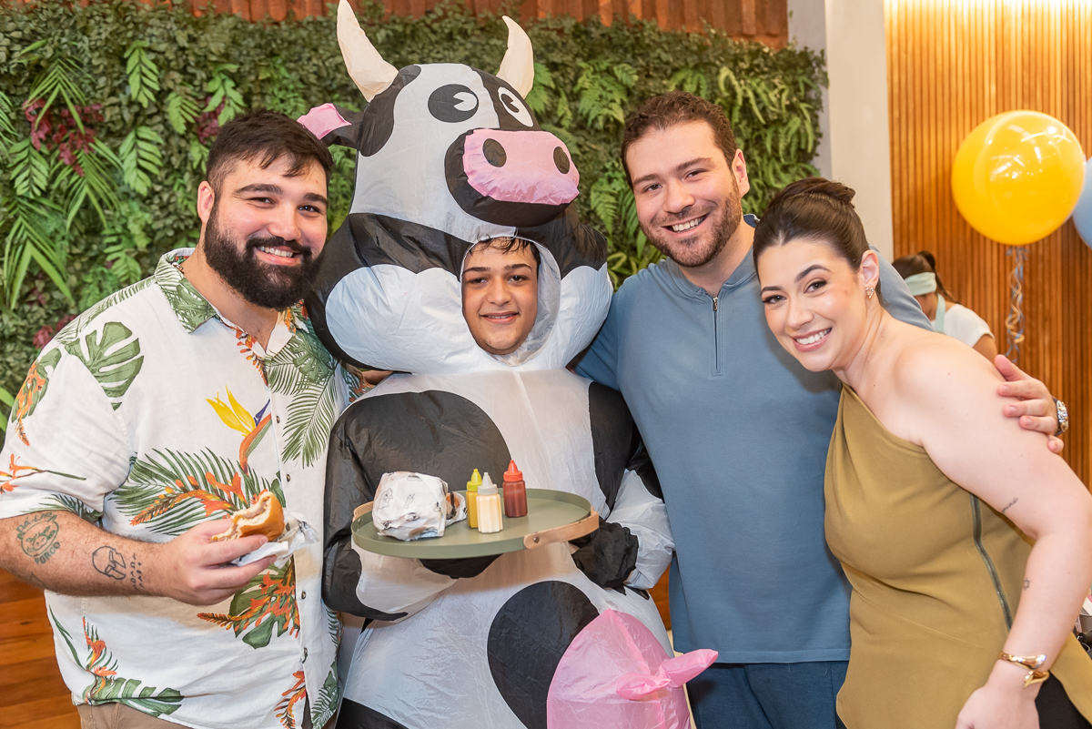 Grupo de adultos, Cowmeburger, Bella Moraes e Jorge Abrão, sorrindo ao lado de animador fantasiado de vaquinha durante festa infantil, momento descontraído de aniversário infantil em buffet com fotografia profissional na Casa Sapoti.
