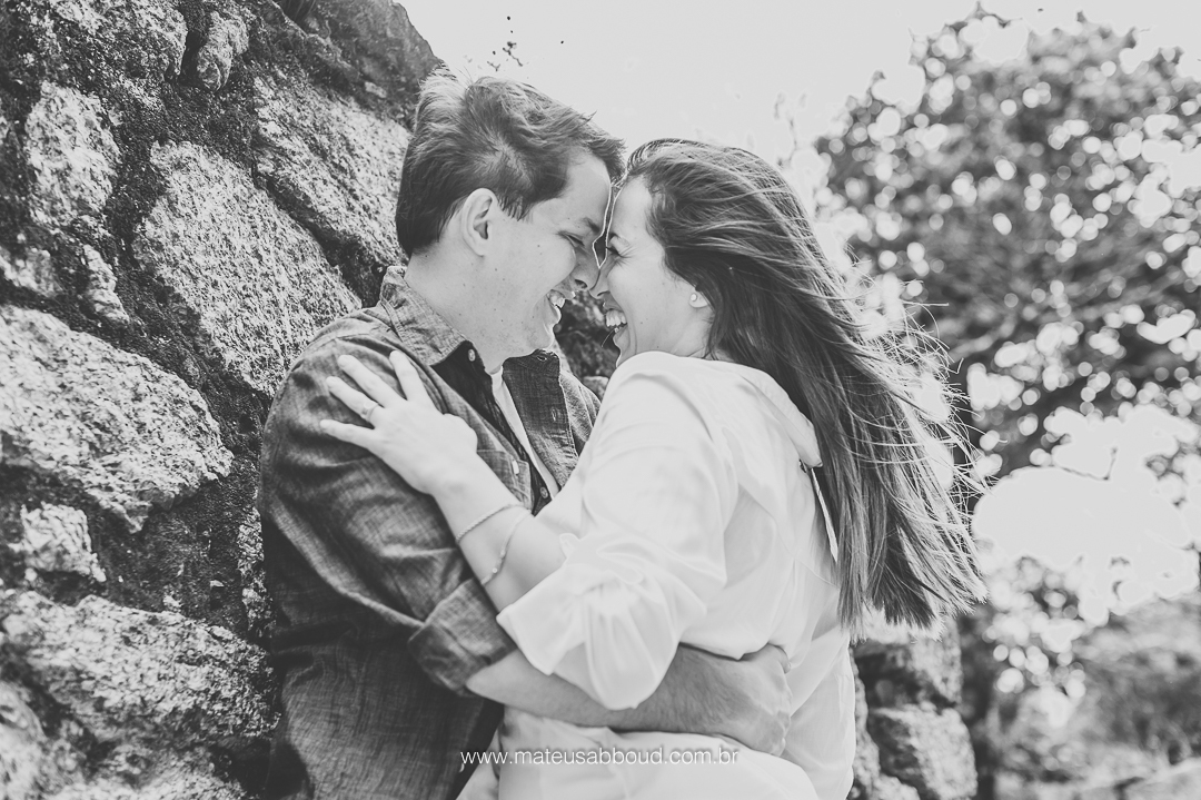 foto em preto e branca. foto de casal. marido de frente pra esposa e abraçando ela pela cintura. As testas estão juntas e ambos estão sorrindo.