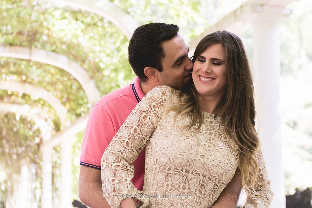 foto de casal com o noivo atrás da noiva beijando o pescoço da noiva e ela rrindo de felicidade no jardim botânico no rio de janeiro rj
 
