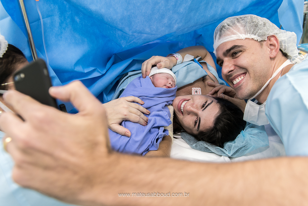 Pai fazendo o primeiro selfie com a mamãe e o bebê ainda na sala de parto.